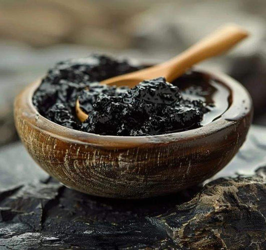 Wooden bowl with black Salajeet resin and wooden spoon on rustic surface