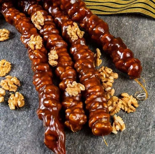 Traditional Walnut Churchkhela sticks coated in rich grape juice with walnut pieces scattered around on a dark surface
